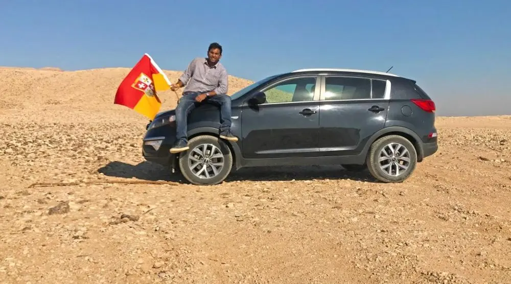 Man with a flag sitting on a car in the desert