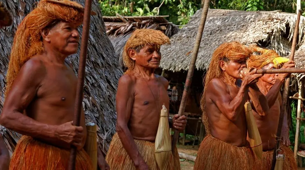 Elders in grass skirts beside thatched huts