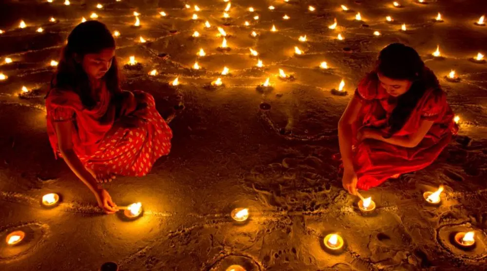 Women lighting rows of oil lamps at night