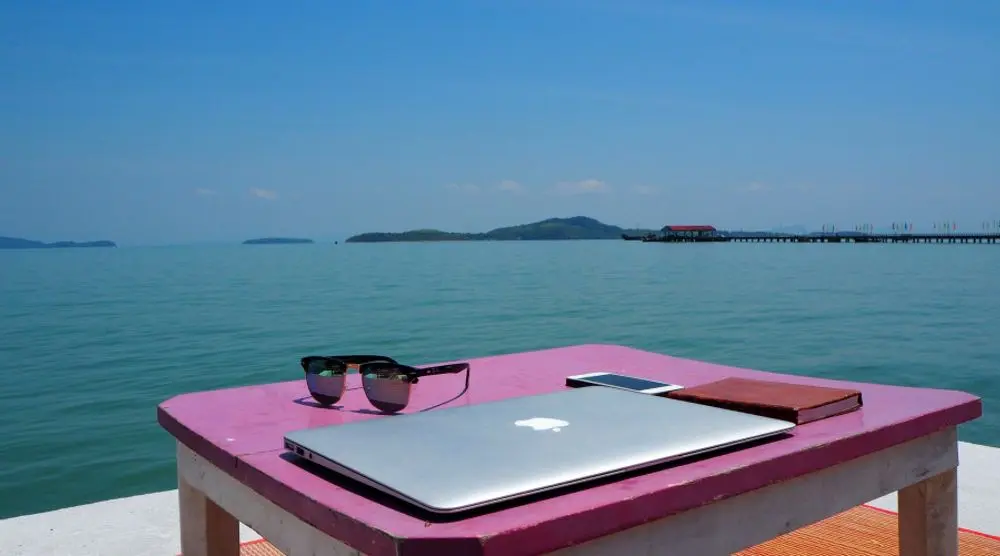 Laptop and sunglasses on a table by the sea