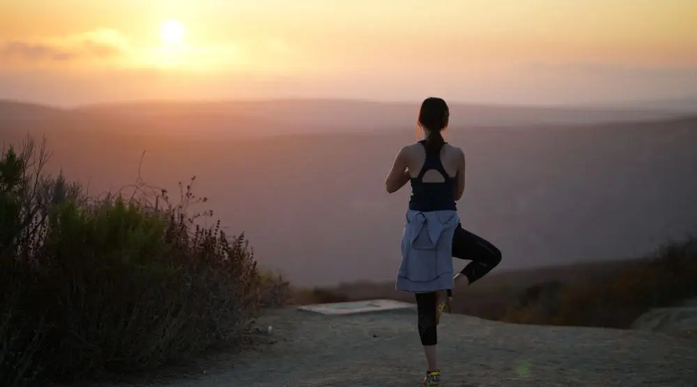 Woman in a yoga pose on a hilltop at sunset