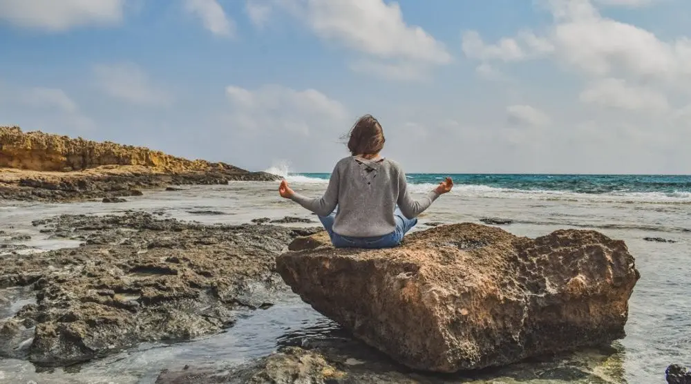 Person meditating on a rock by the sea
