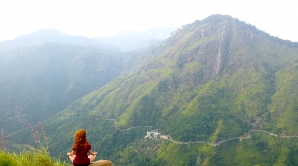 Person meditating on a green mountain ridge