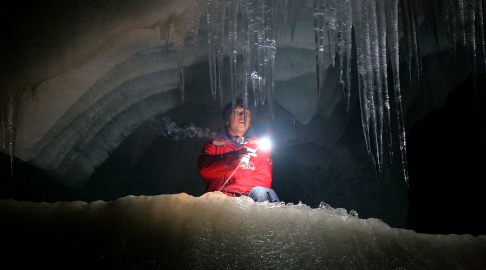Explorer with a lamp among ice formations in Eisriesenwelt